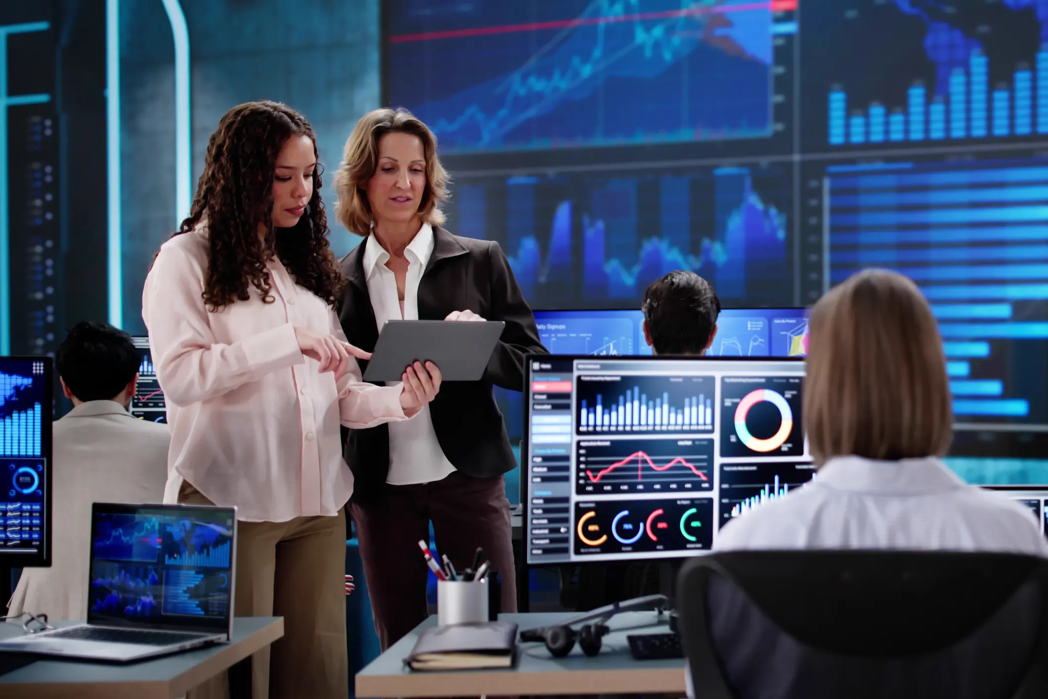 Two women analyzing financial data on digital devices in a modern office.